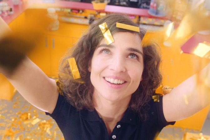 Eine fröhlich lächelnde Michèle Rohrbach mit lockigem Haar und schwarzem Poloshirt schaut nach oben, während goldene Konfettistreifen um sie herum fliegen.