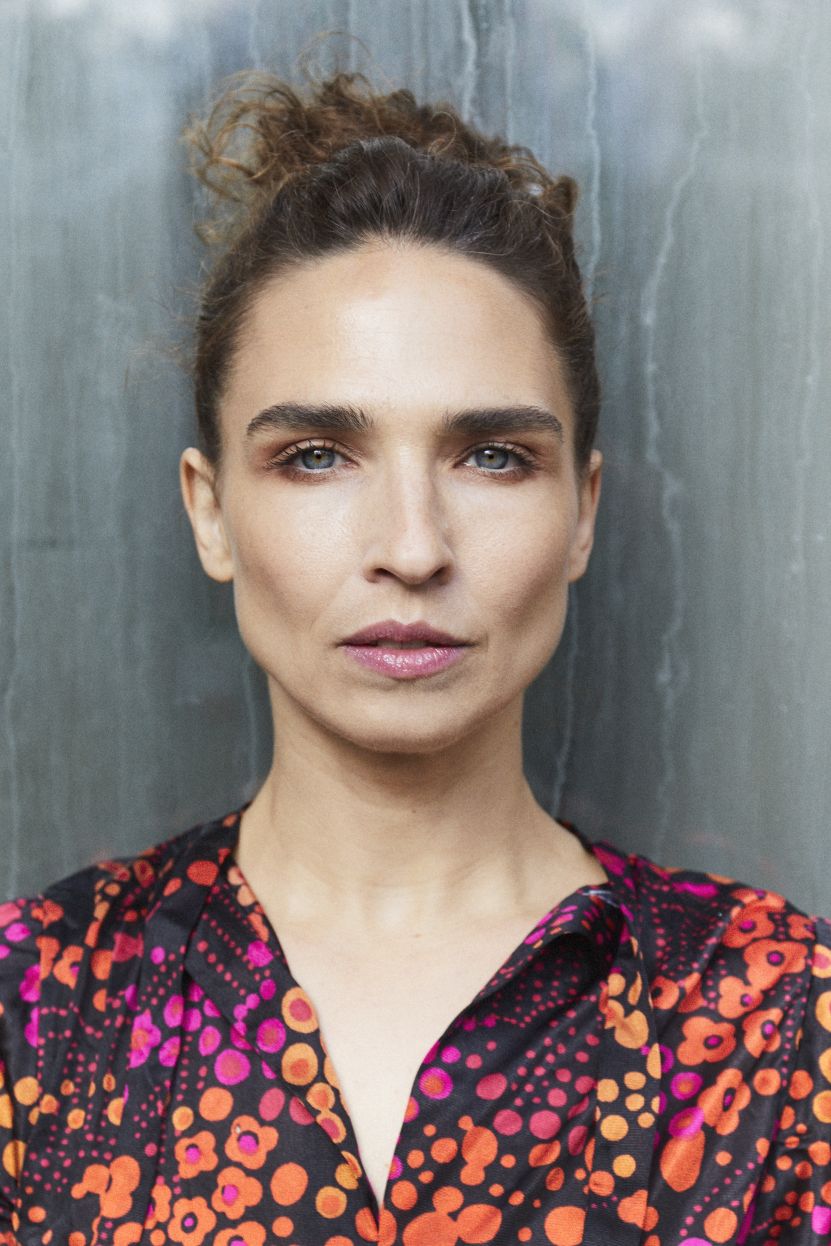 Michèle Rohrbach mit zurückgebundenem Haar blickt direkt in die Kamera. Sie trägt eine farbenfrohe Bluse mit orange-roten und pinken Blumenmustern.